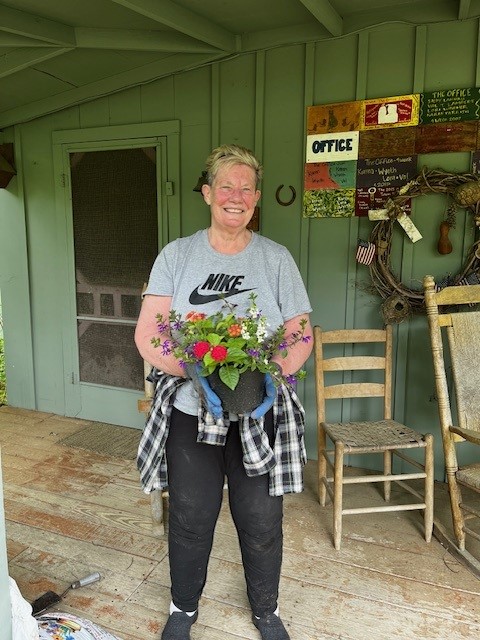 A volunteer holding a flowerpot filled with vibrant blooms on the camp’s welcoming porch.