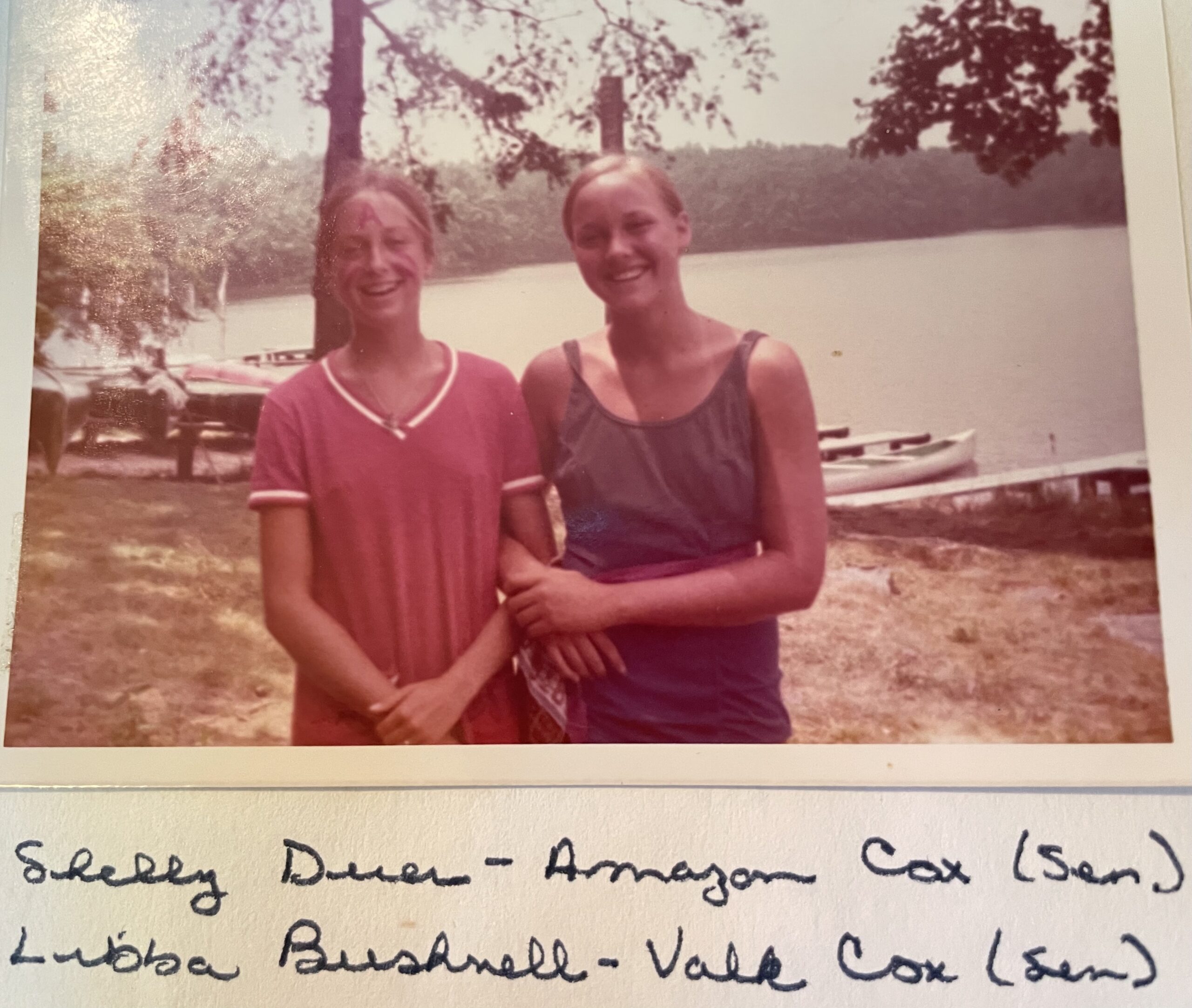 A vintage photo of two smiling campers at Camp Nakanawa standing near Lake Aloaloa Shelly Duer the Amazon War Canoe cox sports a painted A on her foreheadmarking the beginning of a beloved camp tradition