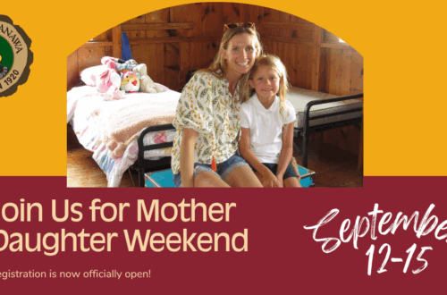 Mother and young daughter sitting together on a bed in a cozy wooden Camp Nakanawa cabin, inviting families to register for Mother Daughter Weekend, September 12–15.